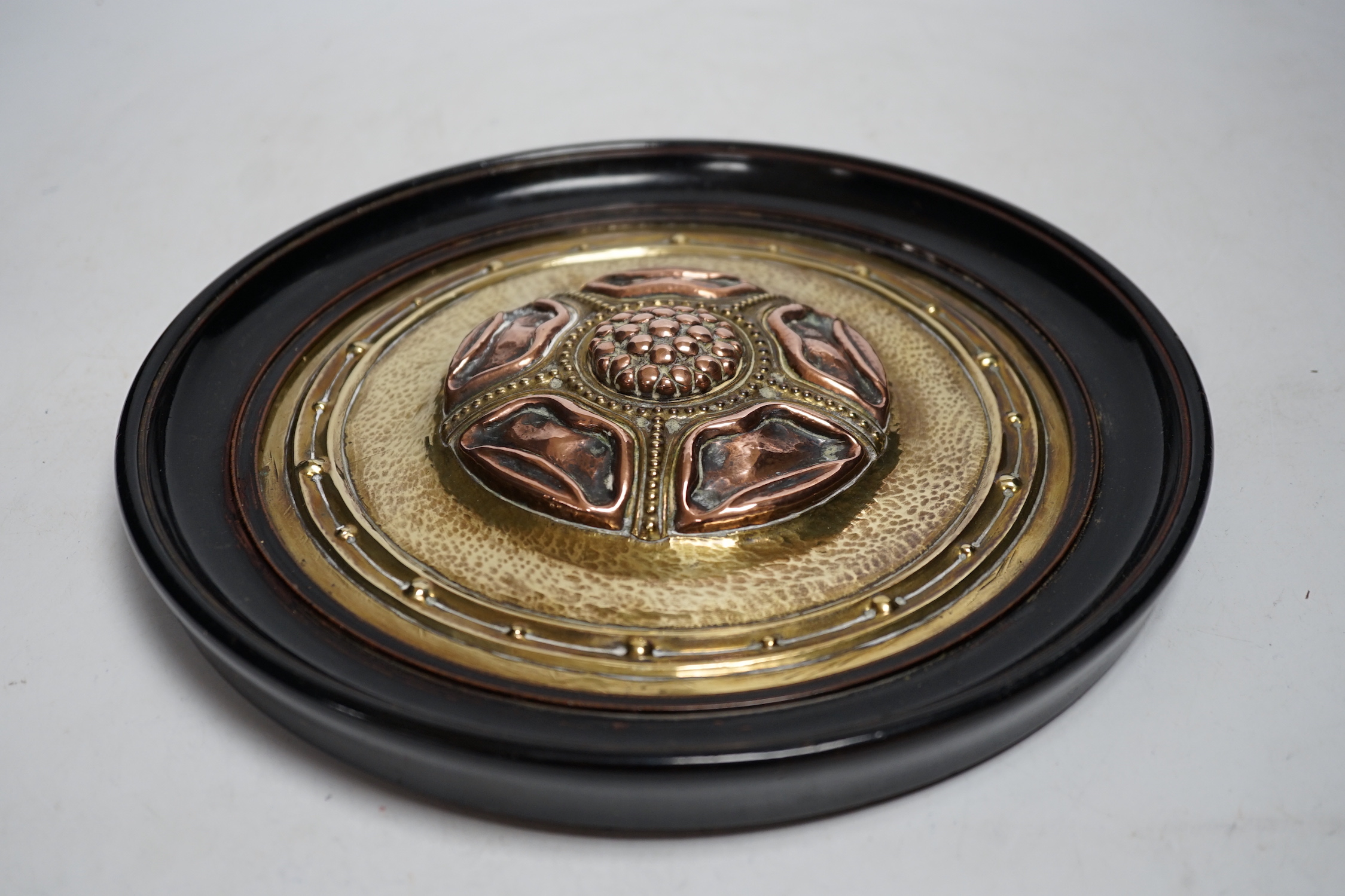 An Arts and Crafts brass and copper roundel, in the manner of Archibald Knox, monogrammed CA, ebony framed, overall 27cm